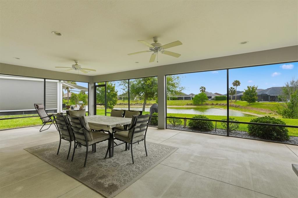 A screened-in patio features a dining set on a rug, ceiling fans, and pond views — 5819 WHITE IBIS RUN, THE VILLAGES, FL