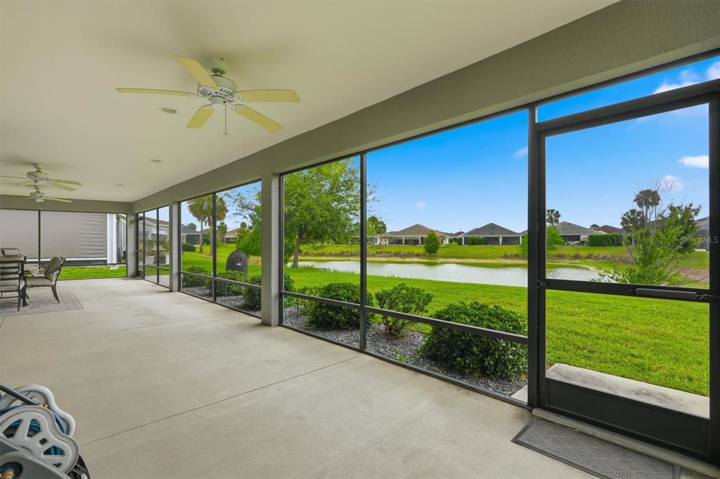 A screened-in patio with ceiling fans overlooks a grassy lawn and a small pond — 5819 WHITE IBIS RUN, THE VILLAGES, FL