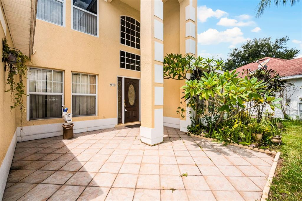 A paved front patio leads to the entrance of a two-story house with yellow stucco — 12422 SION COURT, ORLANDO, FL