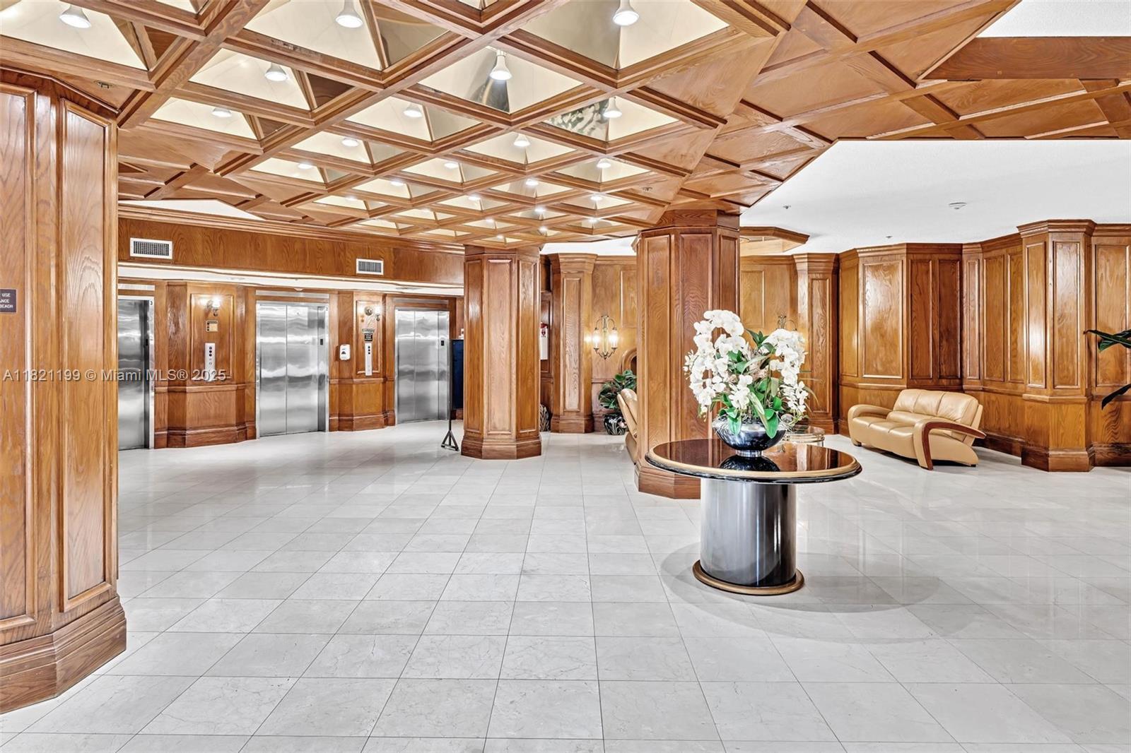 This lobby features wood-paneled walls, a coffered ceiling, a central pedestal table, and elevator doors — 1865 S Ocean Dr # 5J, Hallandale Beach FL 33009, HALLANDALE BEACH, FL