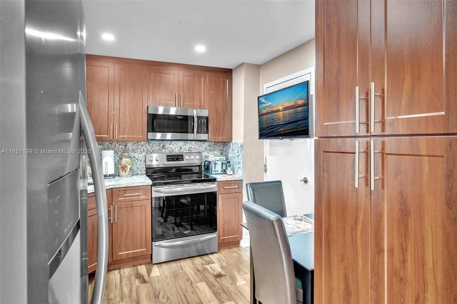 A kitchen features wood cabinets, stainless steel appliances, granite countertops, and a dining area — 1865 S Ocean Dr # 5J, Hallandale Beach FL 33009, HALLANDALE BEACH, FL