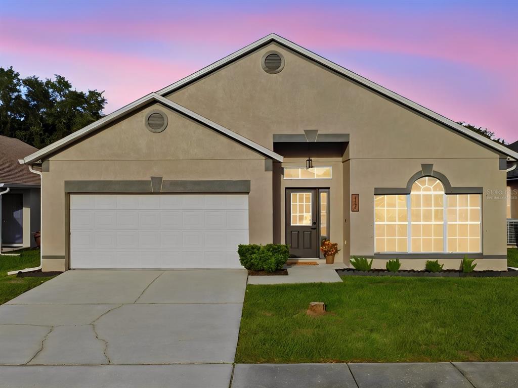A single-story house with a two-car garage, beige stucco exterior, and a front-facing arched window — 2104 MALLARD CREEK CIRCLE, KISSIMMEE, FL