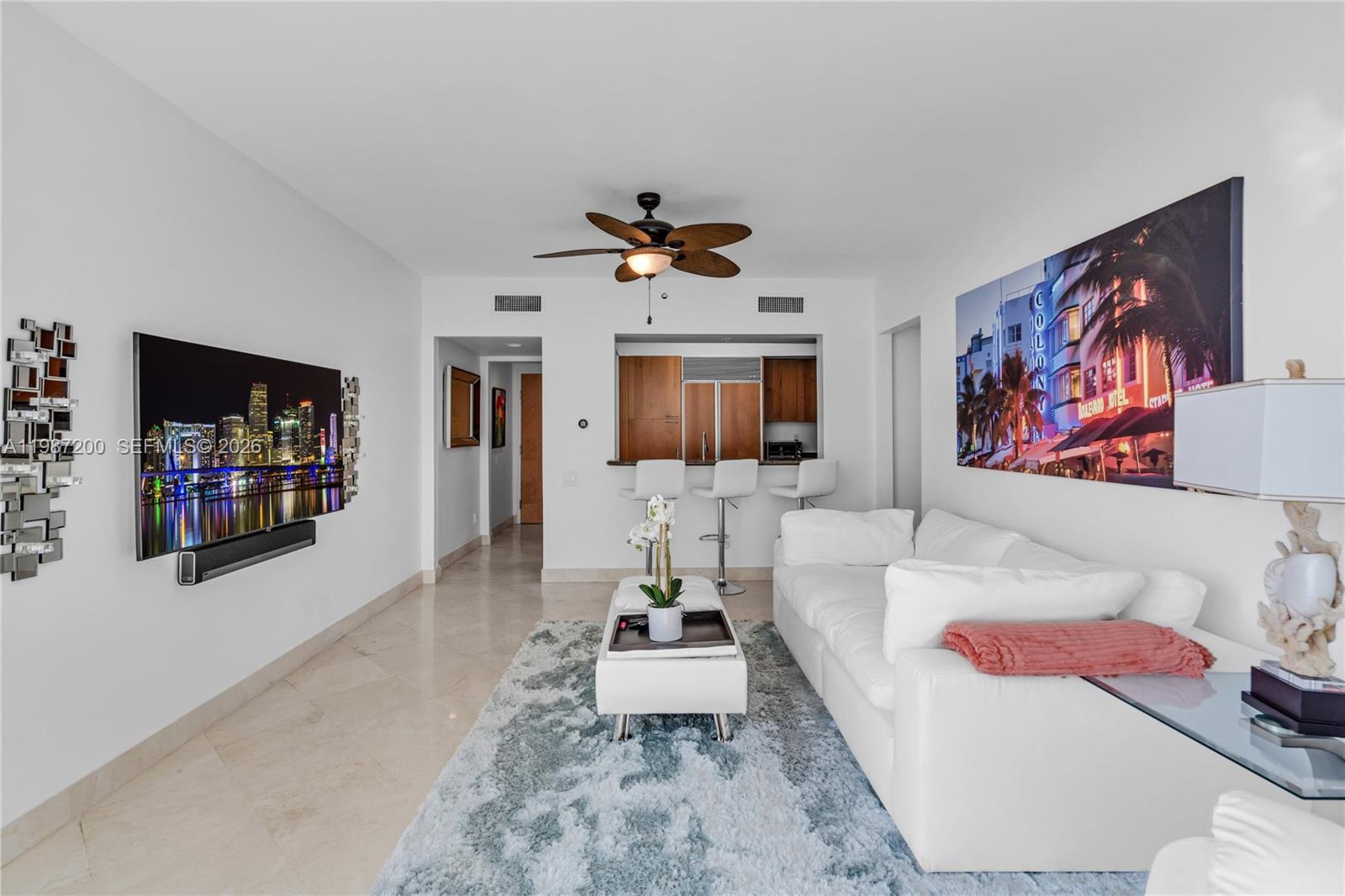 A living room features a white sofa, a television, a rug, and a kitchen pass-through — 1500 Ocean Dr # 907, Miami Beach FL 33139, MIAMI BEACH, FL