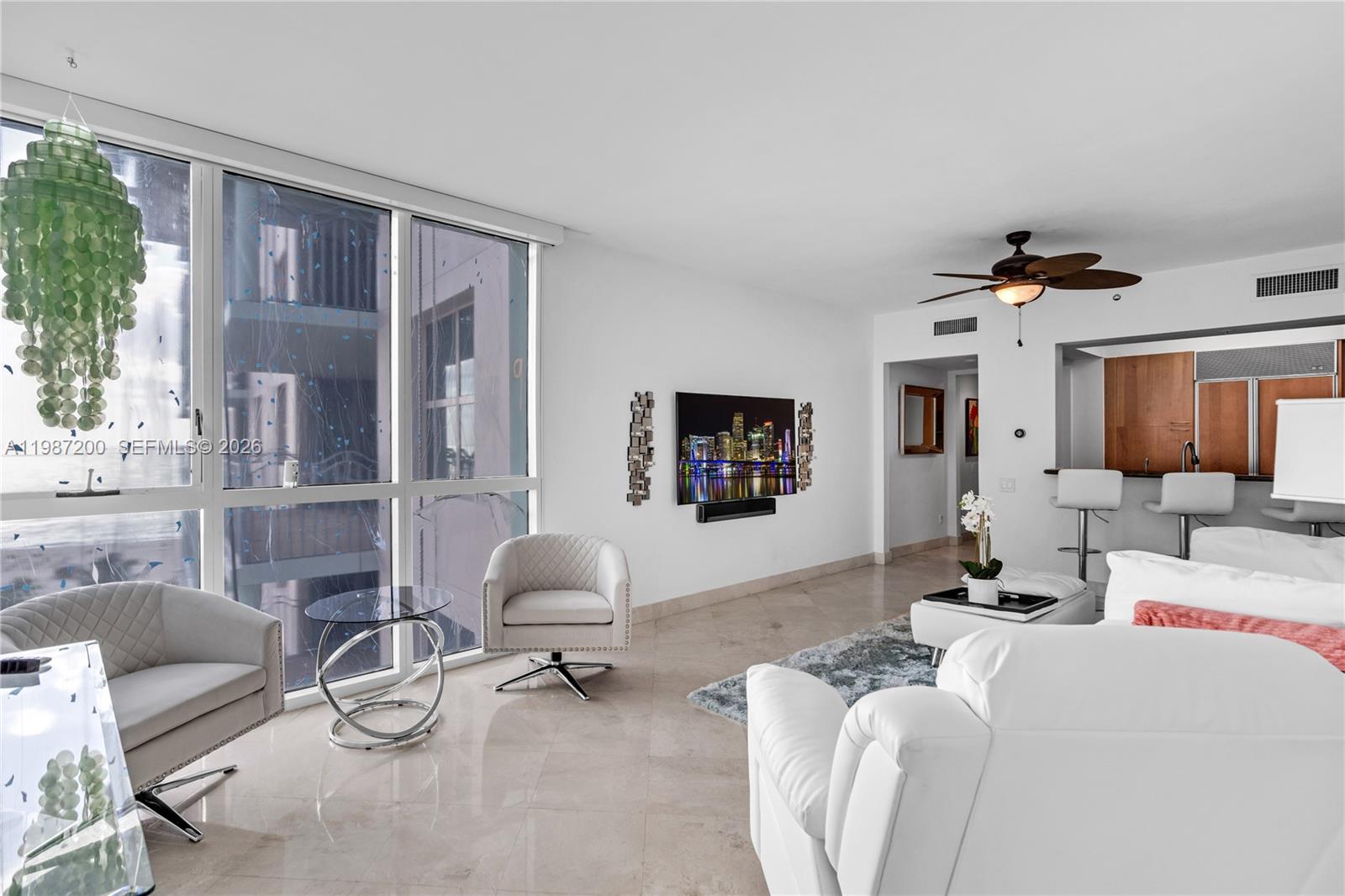 A modern living room features white furniture, a wall-mounted television, and floor-to-ceiling windows — 1500 Ocean Dr # 907, Miami Beach FL 33139, MIAMI BEACH, FL