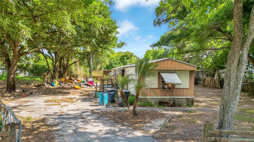 A mobile home sits on a lot with scattered debris and mature trees — 124 6TH WAHNETA STREET W, WINTER HAVEN, FL