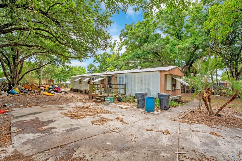 An exterior view of a weathered mobile home with a concrete driveway and surrounding trees — 124 6TH WAHNETA STREET W, WINTER HAVEN, FL