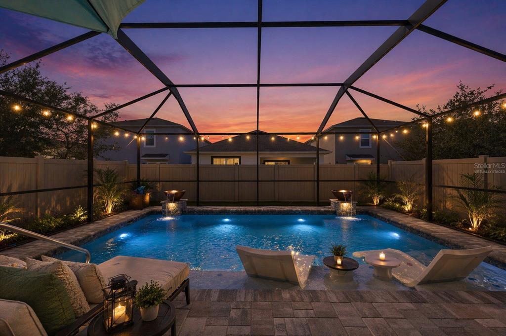 A screened-in backyard pool with lounge chairs, water features, and string lights at sunset — 32756 ANSLEY BLOOM LANE, WESLEY CHAPEL, FL