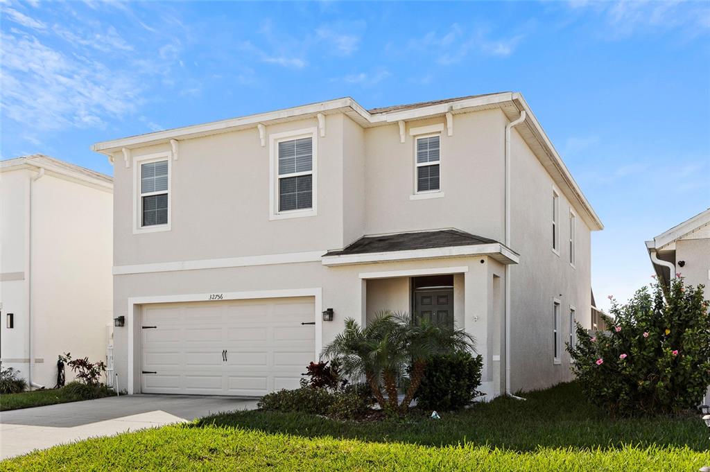 A two-story, light-colored stucco house features a two-car garage and a front entrance — 32756 ANSLEY BLOOM LANE, WESLEY CHAPEL, FL