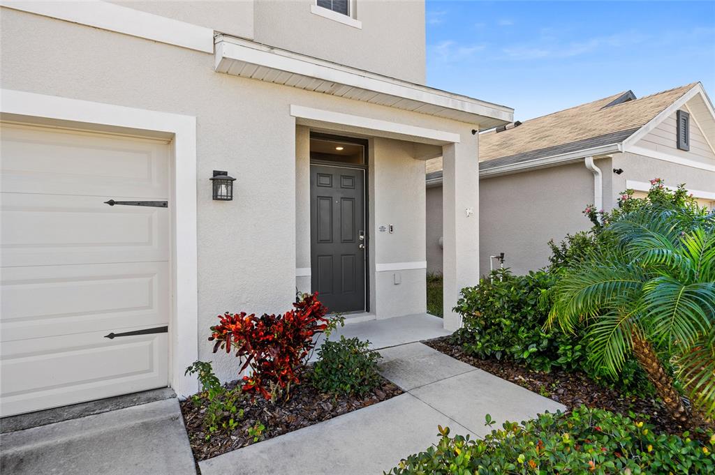 The exterior of a house features a gray front door, a garage, and landscaping — 32756 ANSLEY BLOOM LANE, WESLEY CHAPEL, FL
