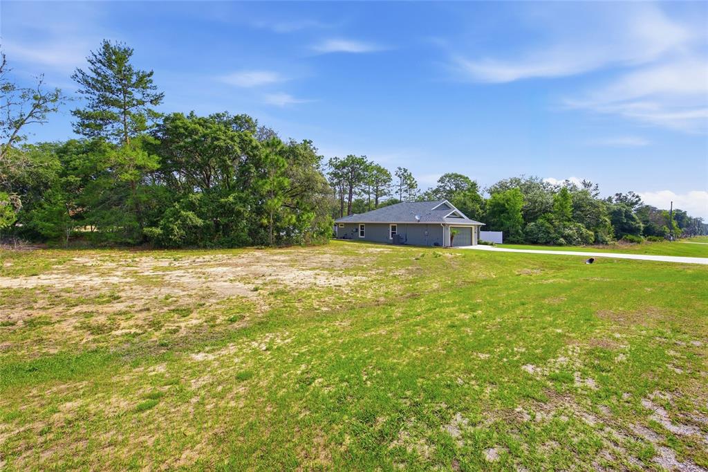 A gray house sits on a large, grassy lot surrounded by trees under a blue sky — 141 FISHER WAY, OCKLAWAHA, FL