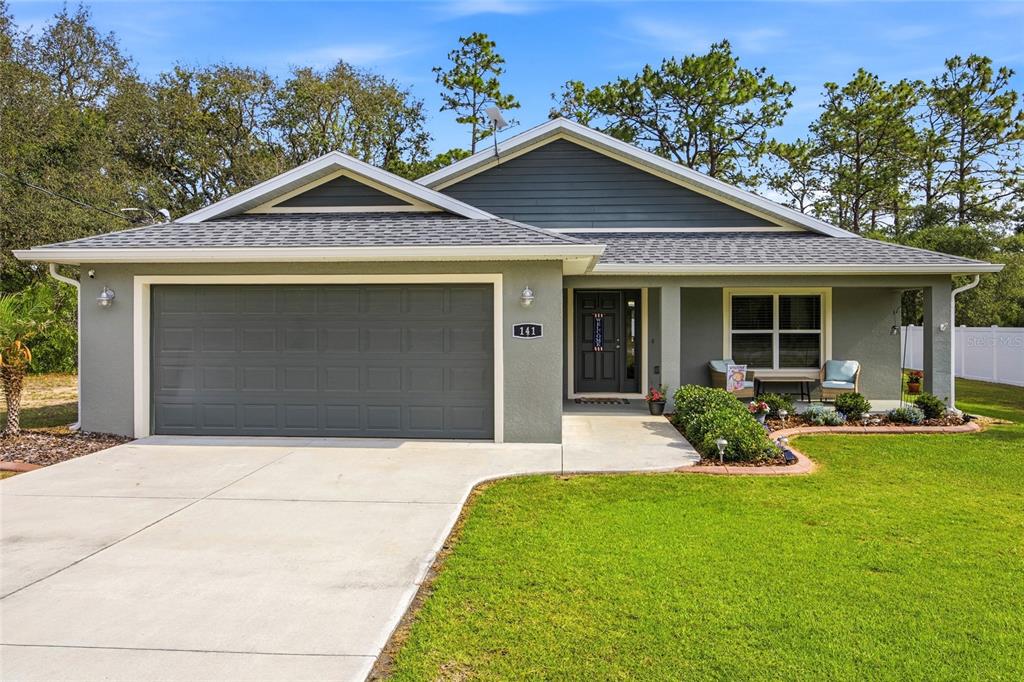 A single-story house with a gray stucco exterior, a two-car garage, and a covered entryway — 141 FISHER WAY, OCKLAWAHA, FL