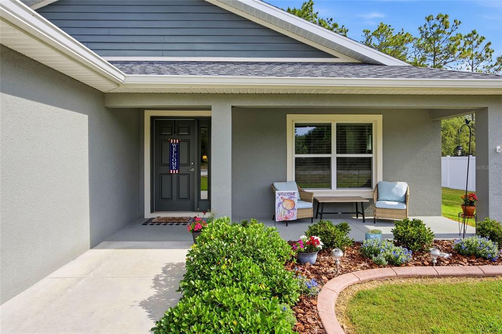 The exterior of a gray house features a covered porch, a front door, and landscaping — 141 FISHER WAY, OCKLAWAHA, FL