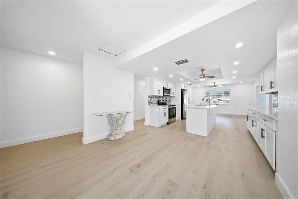 A bright, open-concept kitchen features white cabinetry, a central island, and light wood flooring — 5040 GALLEON COURT, NEW PORT RICHEY, FL