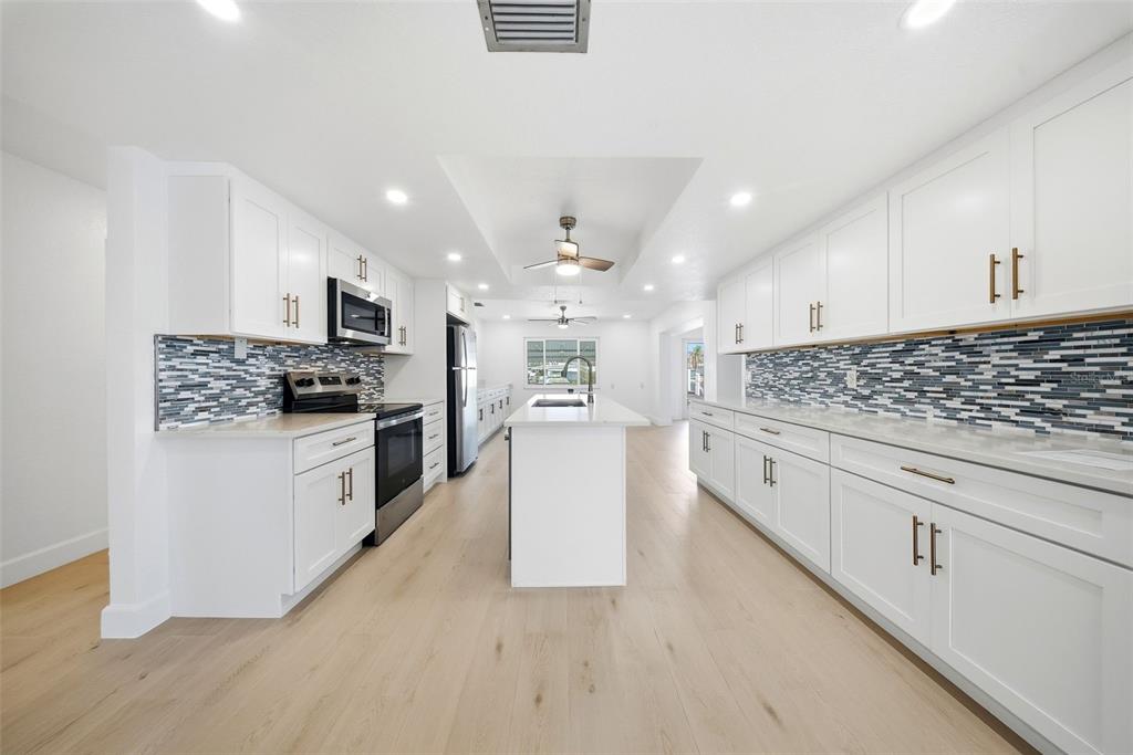 A modern kitchen features white cabinets, a central island, and a blue-toned mosaic tile backsplash — 5040 GALLEON COURT, NEW PORT RICHEY, FL
