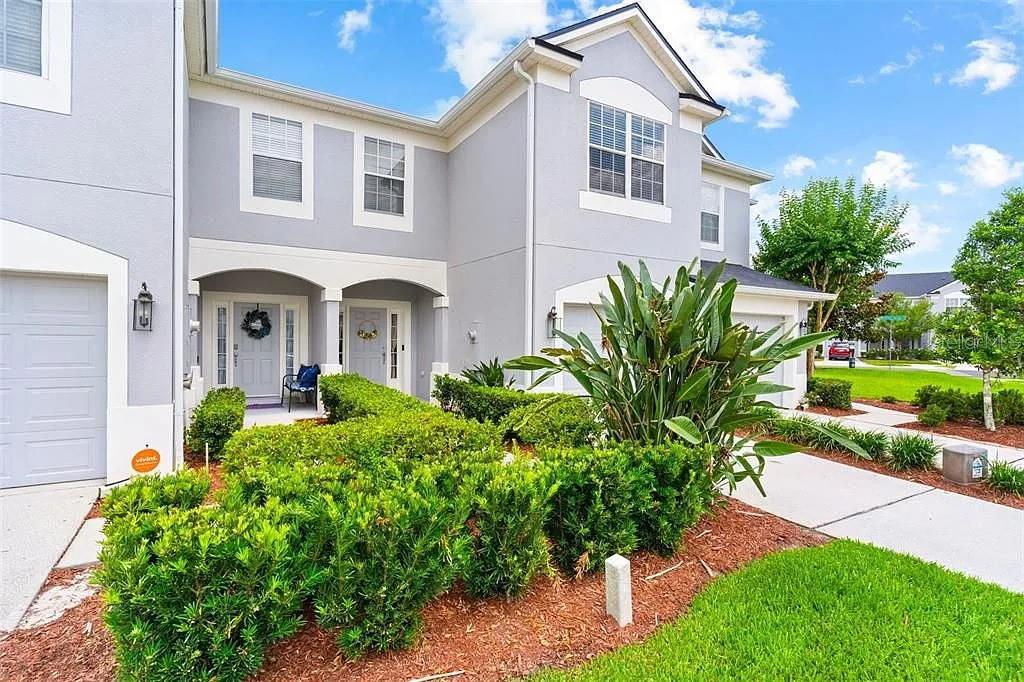 A two-story gray townhouse with a front garden, two entry doors, and a garage — 1115 ROCK HARBOR AVENUE, ORLANDO, FL