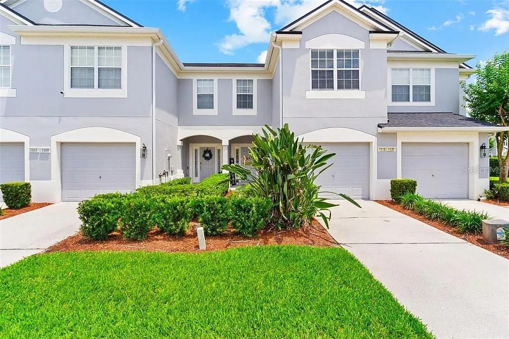 A two-story townhouse exterior with two garages, light gray siding, and a landscaped front yard — 1115 ROCK HARBOR AVENUE, ORLANDO, FL