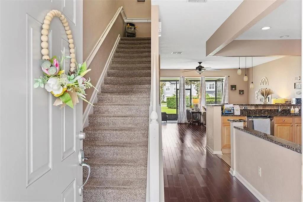 An entryway with a carpeted staircase leads to an open-concept kitchen and living area — 1115 ROCK HARBOR AVENUE, ORLANDO, FL