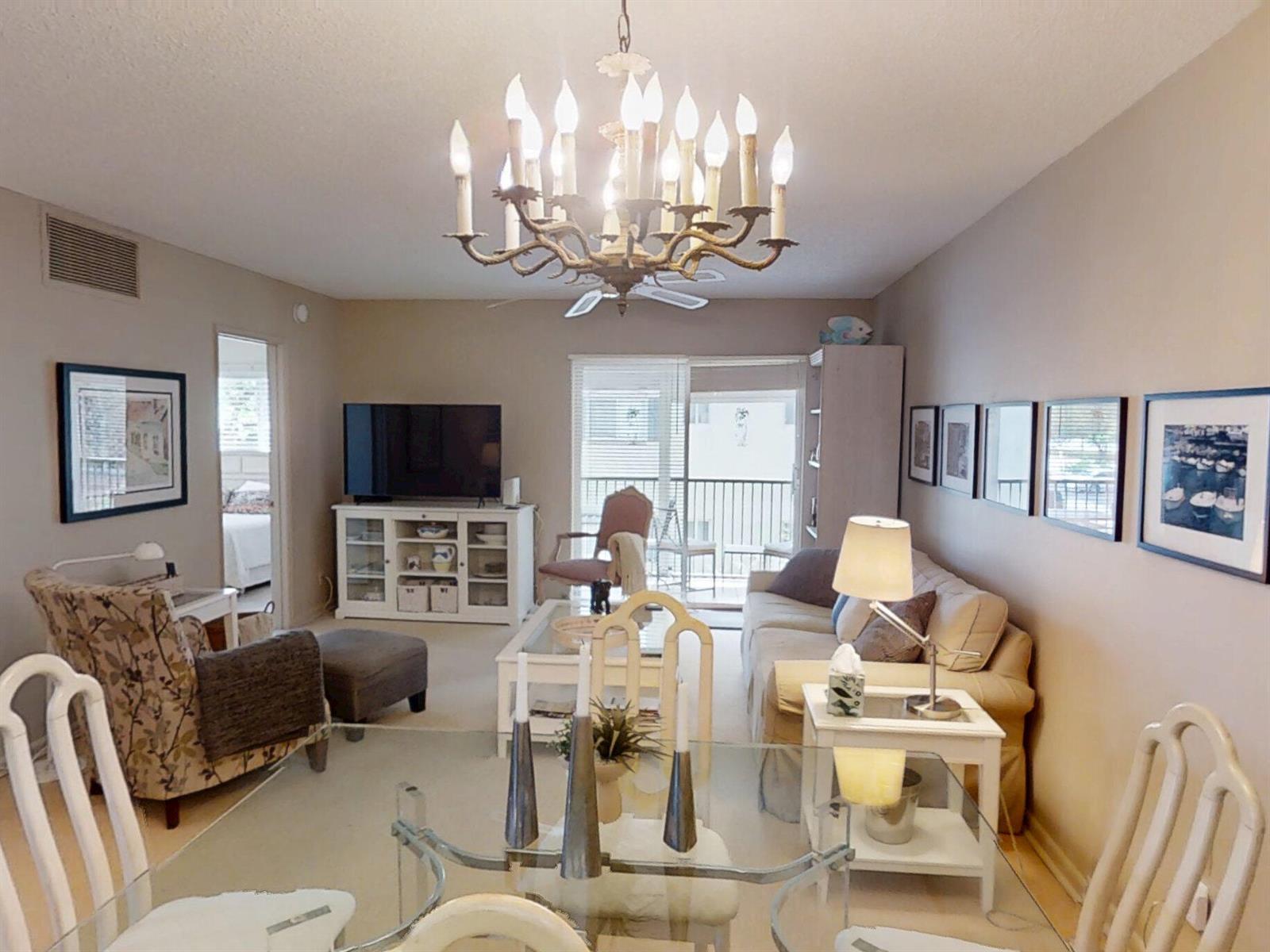 A living room and dining area featuring a large chandelier, neutral walls, and glass furniture — 259 S Cypress Road # 533, Pompano Beach FL 33060, POMPANO BEACH, FL