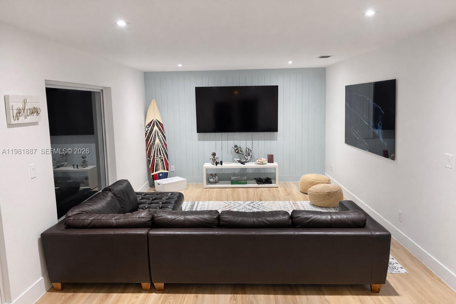 A living room features a dark leather sectional, a wall-mounted television, and light wood flooring — 1240 Binney Dr, Fort Pierce FL 34949, FORT PIERCE, FL