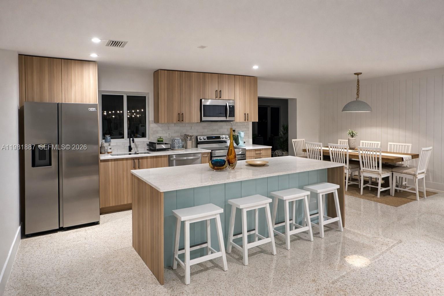 A modern kitchen features light wood cabinets, a blue island with bar stools, and terrazzo flooring — 1240 Binney Dr, Fort Pierce FL 34949, FORT PIERCE, FL