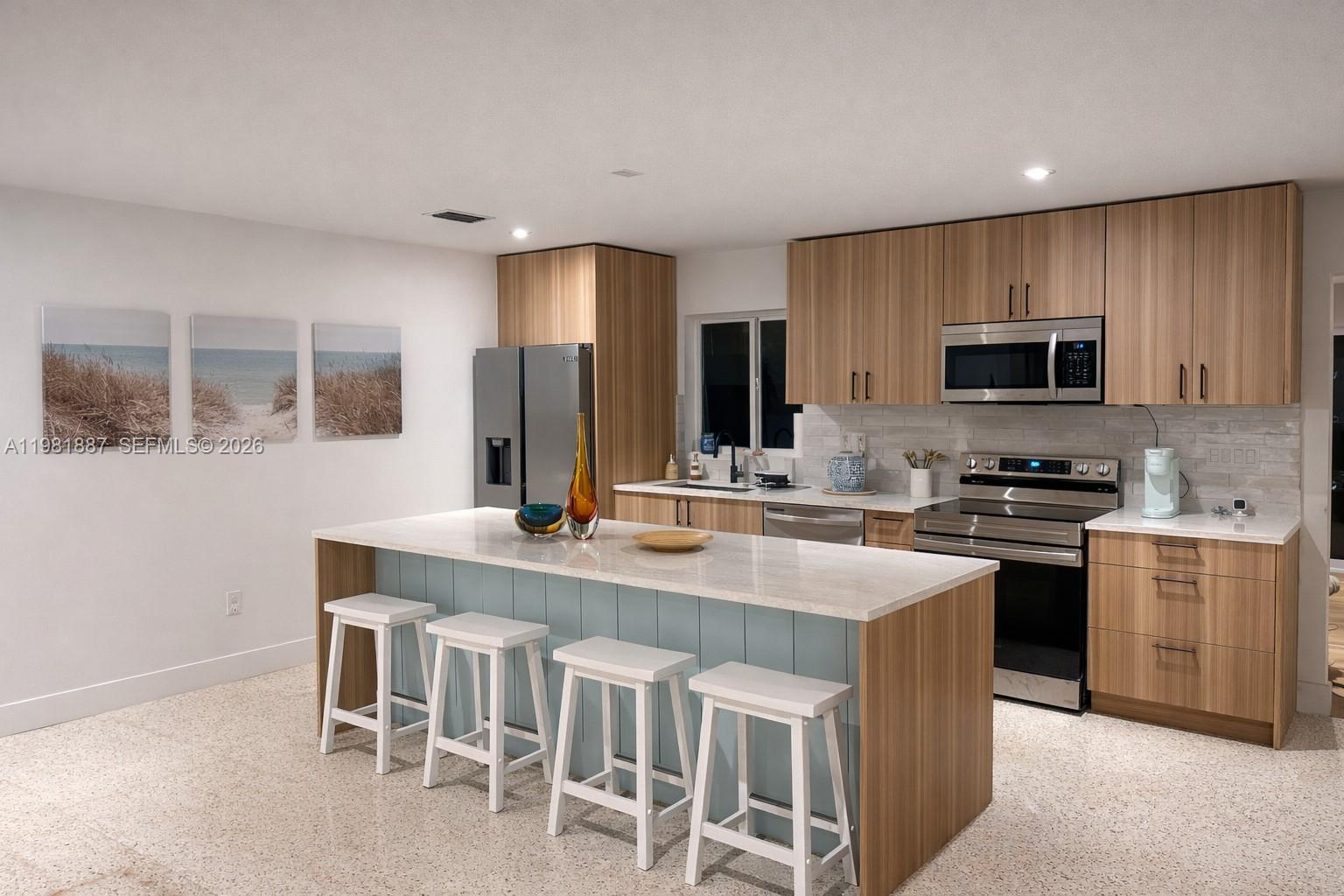 A modern kitchen features wood-grain cabinets, a light blue island with bar stools, and stainless appliances — 1240 Binney Dr, Fort Pierce FL 34949, FORT PIERCE, FL