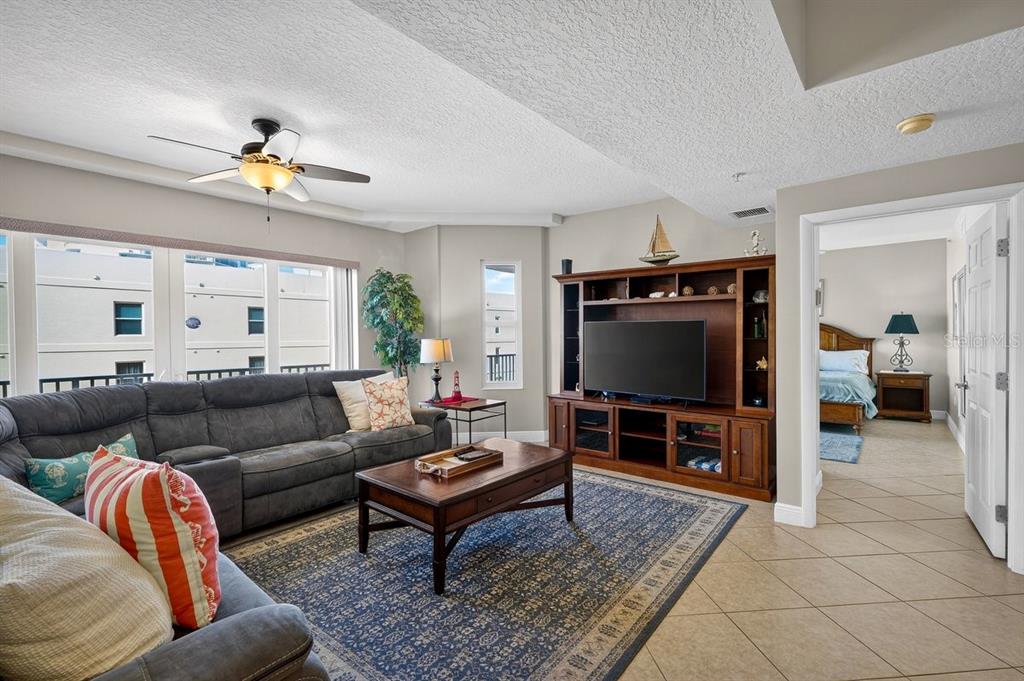 A living room features a gray sectional sofa, a wooden entertainment center, and tile flooring — 3799 S ATLANTIC AVENUE UNIT 601, DAYTONA BEACH SHORES, FL