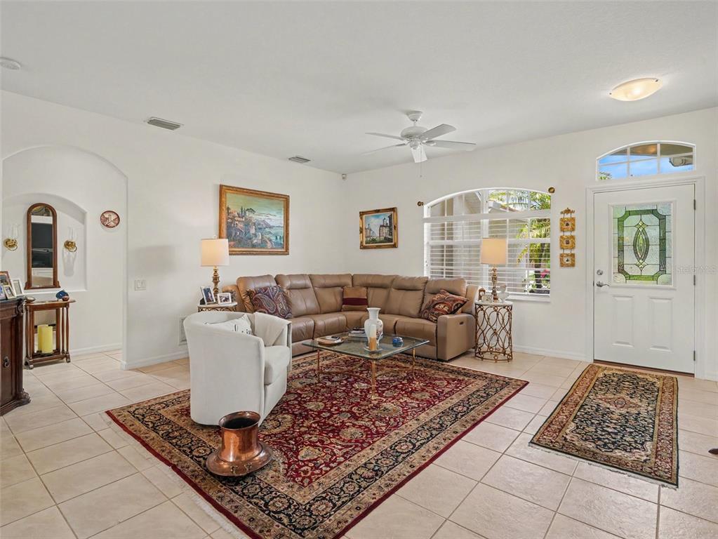 A living room features a tan sectional sofa, a large red area rug, and tile flooring — 2885 ROYAL PALM DRIVE, NORTH PORT, FL