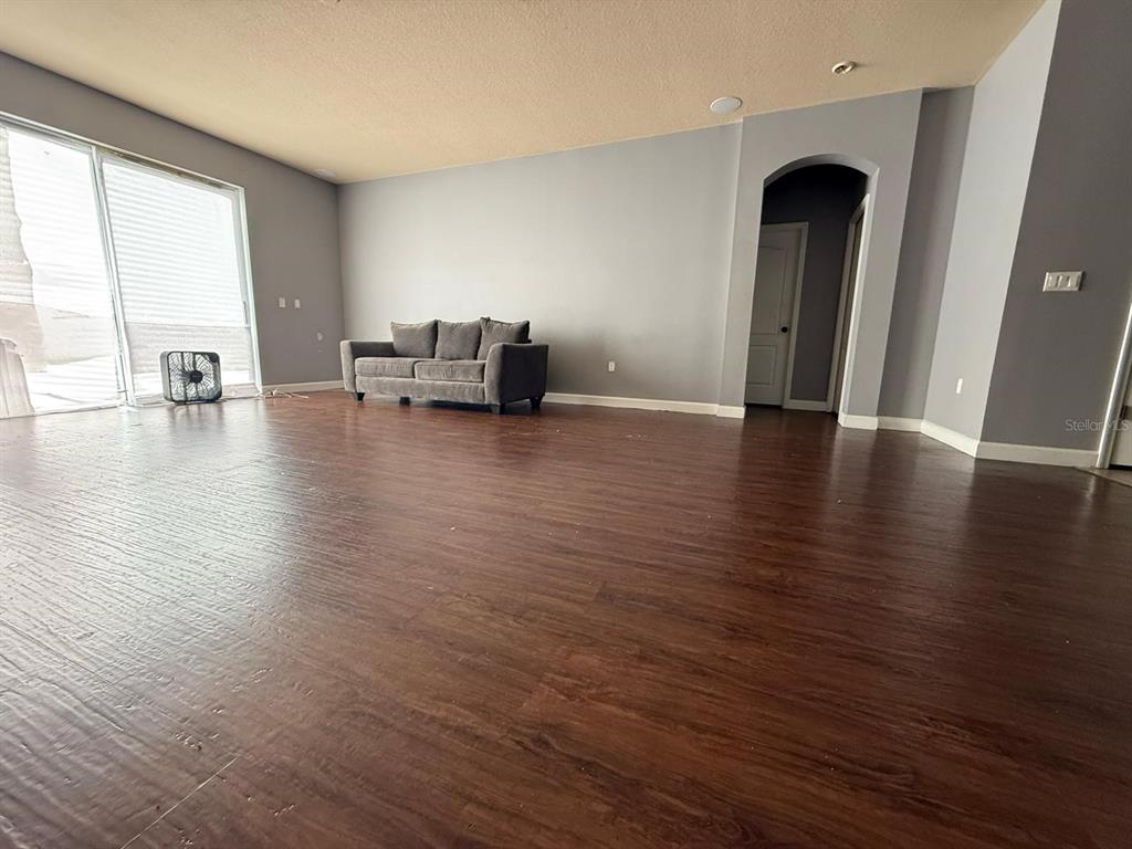 A living room features dark wood-look flooring, gray walls, a gray sofa, and sliding glass doors — 2101 VIA NAPOLI STREET, PLANT CITY, FL