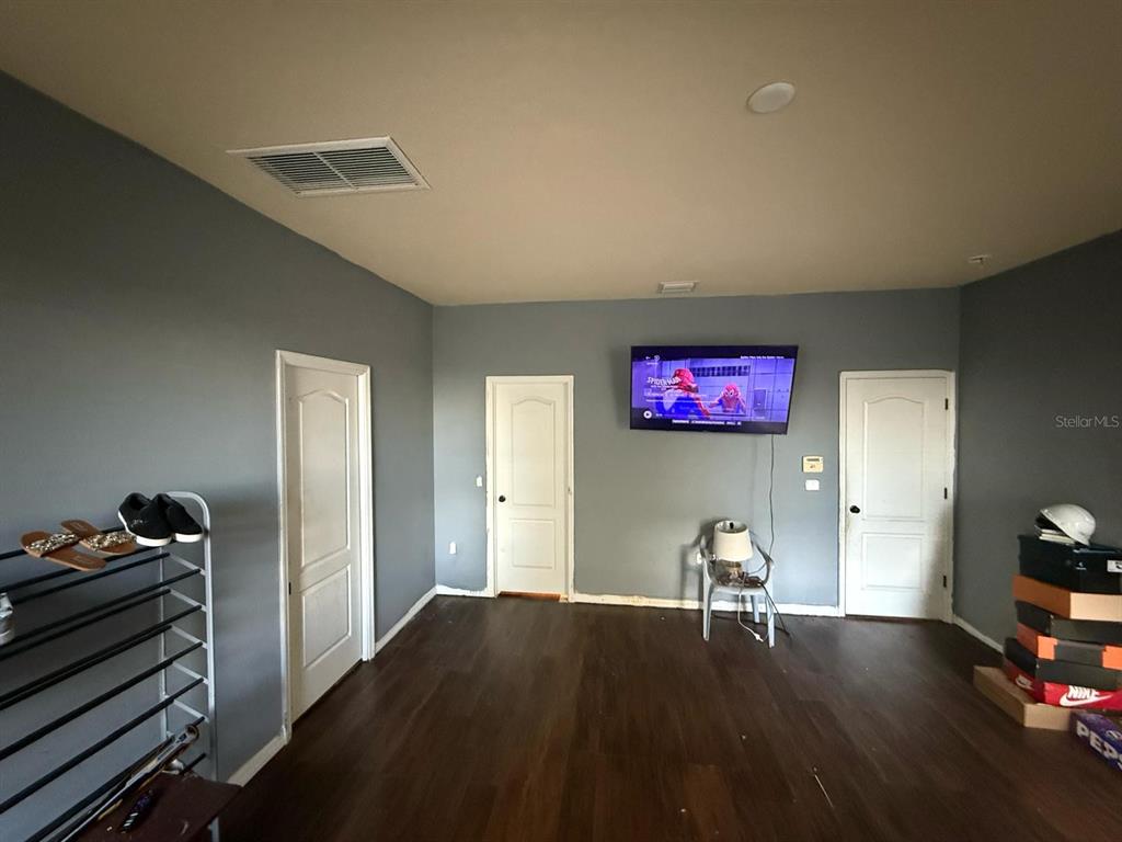 A room with gray walls, dark wood flooring, three white doors, and a wall-mounted television — 2101 VIA NAPOLI STREET, PLANT CITY, FL