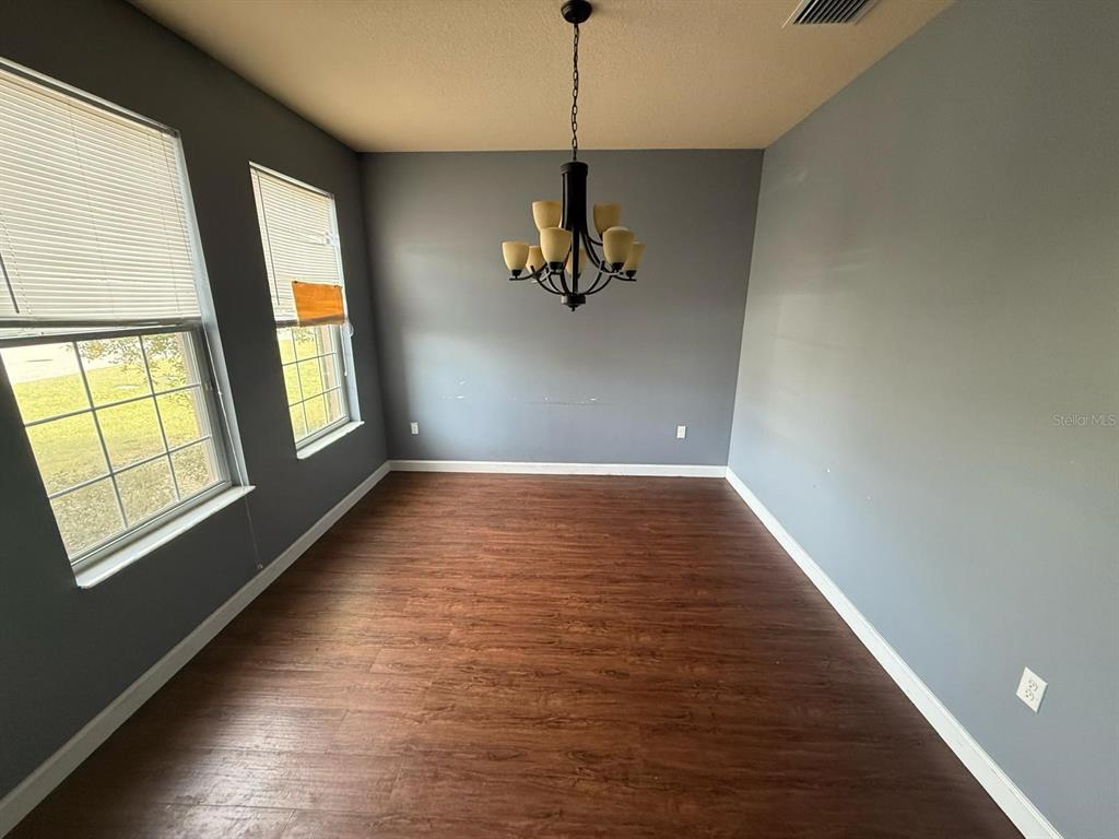 An empty dining room features gray walls, wood-look flooring, and a dark metal chandelier — 2101 VIA NAPOLI STREET, PLANT CITY, FL