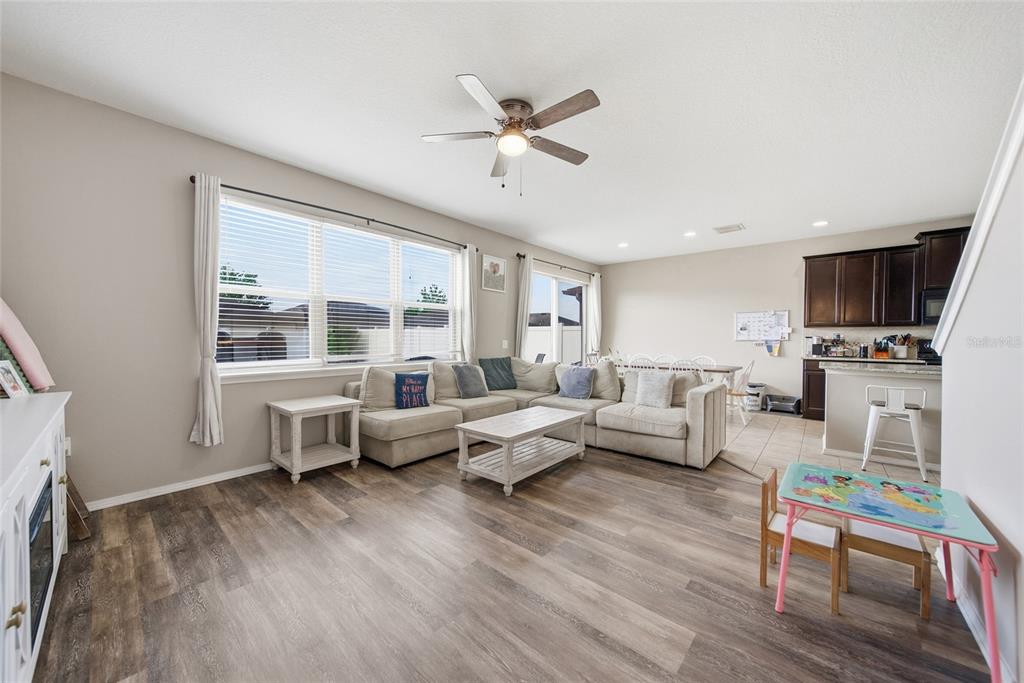 An open-concept living room features wood-look flooring, a sectional sofa, and an adjacent kitchen — 15476 STONE HOUSE DRIVE, BROOKSVILLE, FL