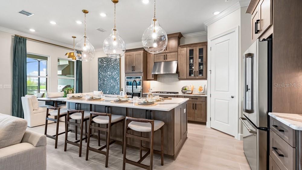 A modern kitchen features a large island with bar seating, wood cabinetry, and pendant lighting — 13450 MANAROLA WAY, ENGLEWOOD, FL