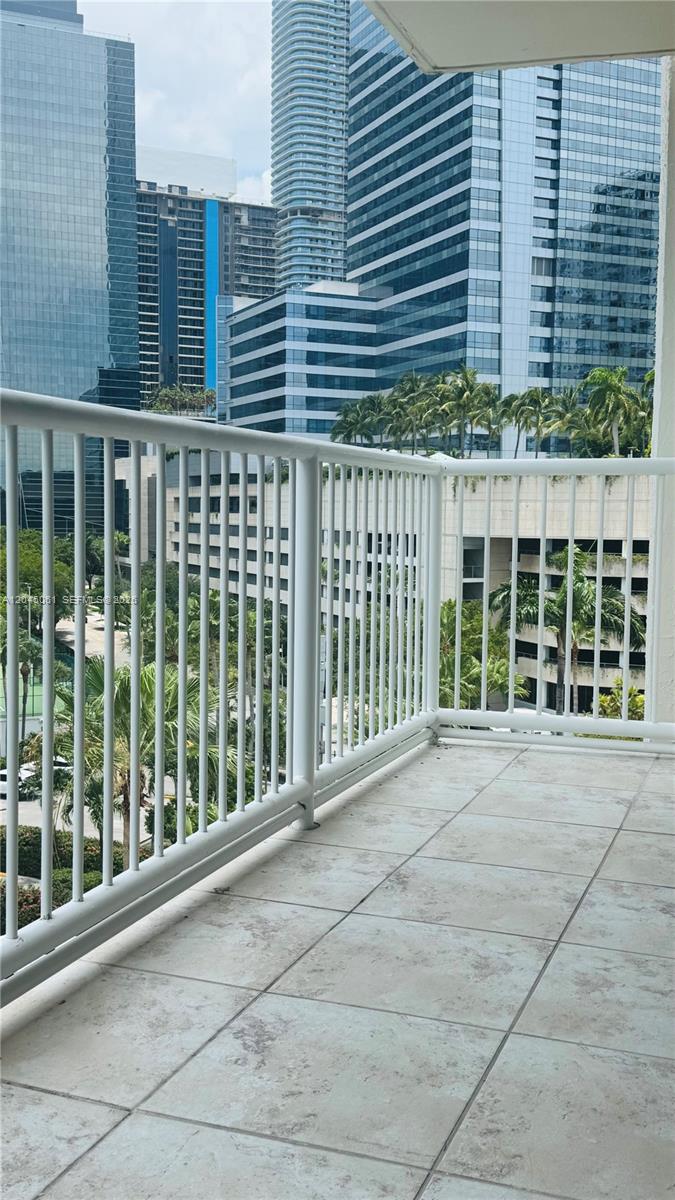 A balcony with white railings overlooks a city skyline with tall glass buildings and palm trees — 1440 Brickell Bay Dr # 810, Miami FL 33131, MIAMI, FL