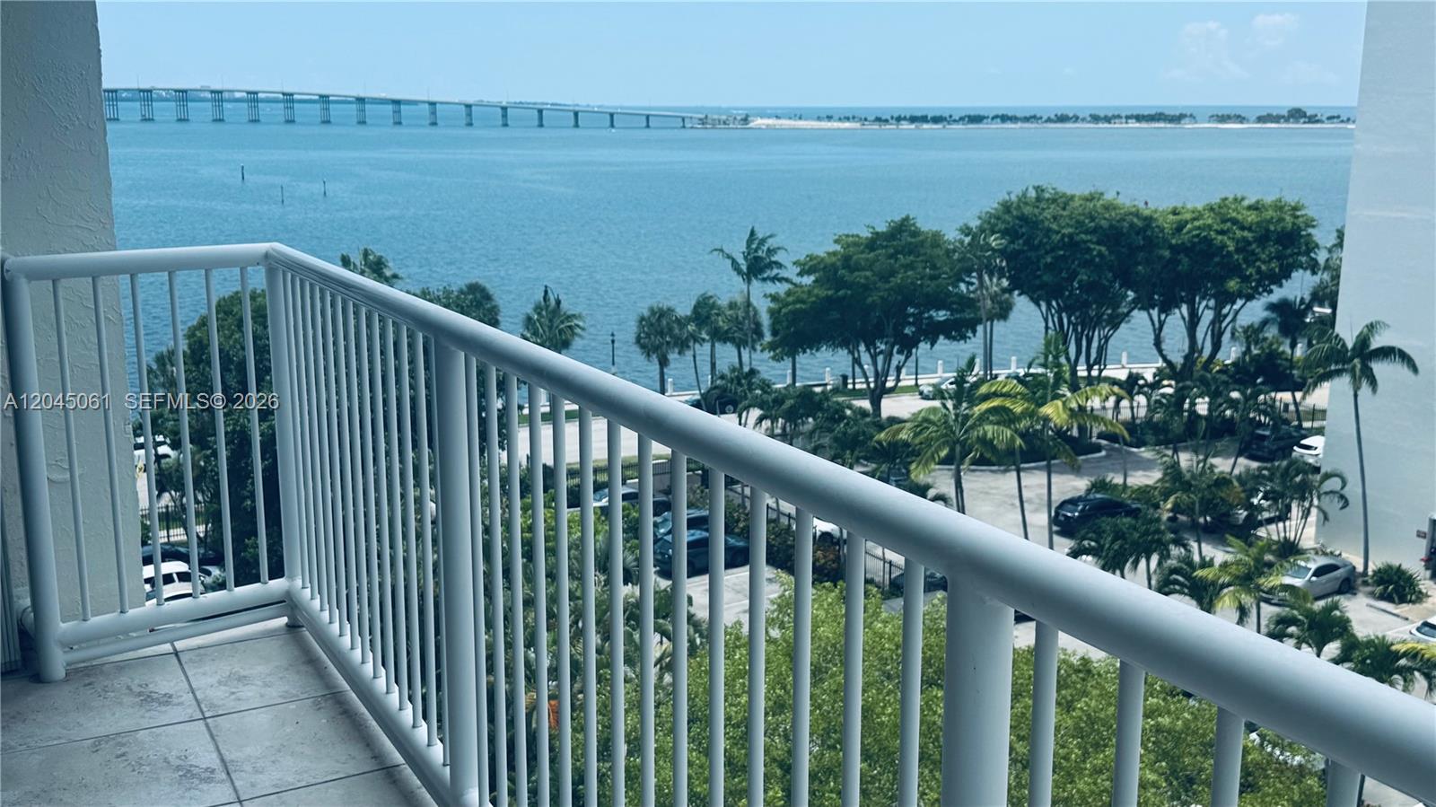 A balcony with a white railing overlooks a parking lot, palm trees, and a bridge — 1440 Brickell Bay Dr # 810, Miami FL 33131, MIAMI, FL