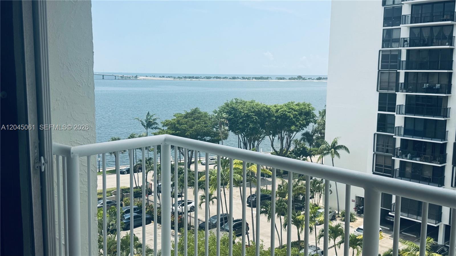 A balcony view overlooks a parking lot, palm trees, and a body of water — 1440 Brickell Bay Dr # 810, Miami FL 33131, MIAMI, FL