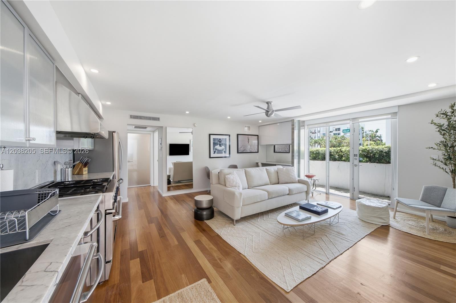 An open-concept living room and kitchen with hardwood floors, a white sofa, and balcony access — 1601 West Ave # 101, Miami Beach FL 33139, MIAMI BEACH, FL