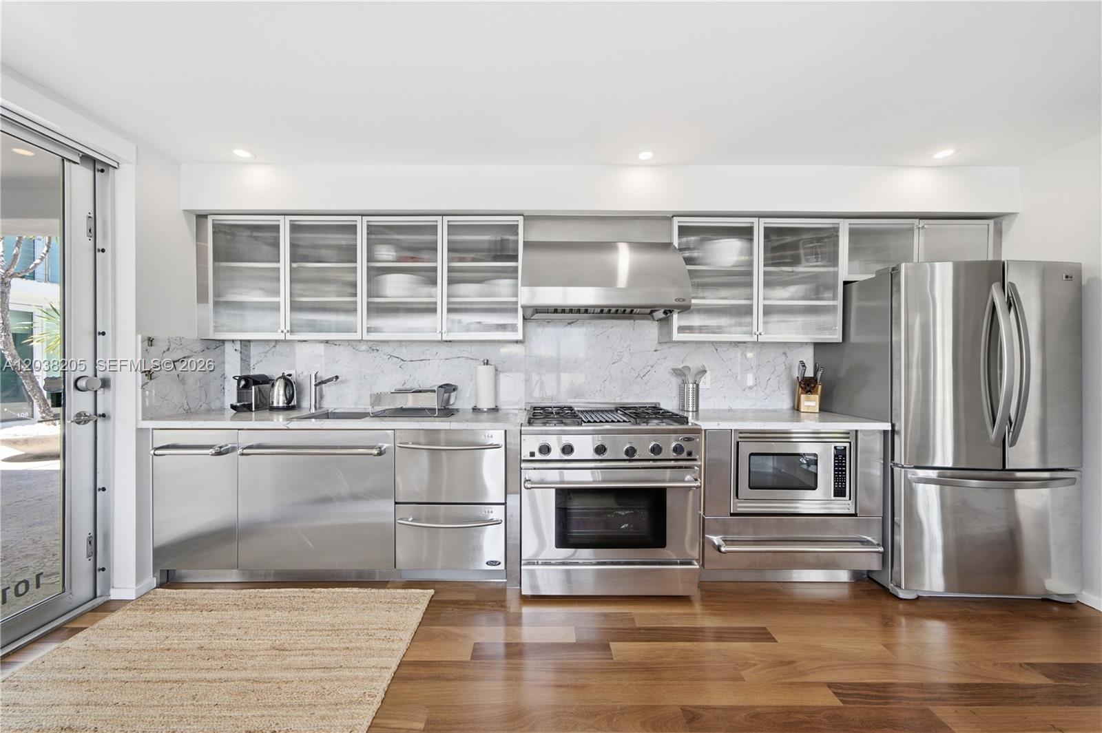 A modern kitchen features stainless steel appliances, marble countertops, and glass-front upper cabinets — 1601 West Ave # 101, Miami Beach FL 33139, MIAMI BEACH, FL