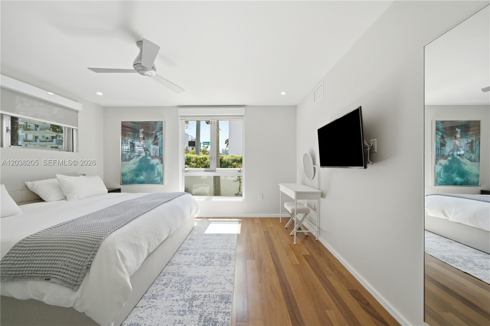 A bedroom features a bed, a wall-mounted television, a vanity, and hardwood flooring — 1601 West Ave # 101, Miami Beach FL 33139, MIAMI BEACH, FL