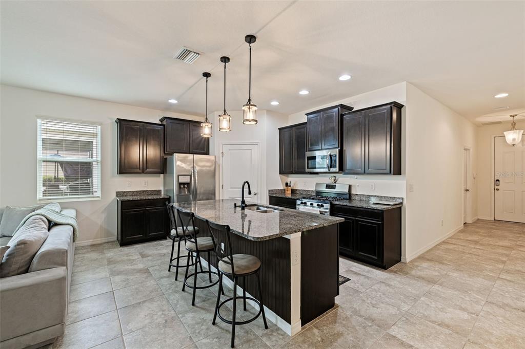 A kitchen with dark cabinets, granite countertops, a center island with seating, and tile flooring — 7533 LANTERN PARK AVENUE, APOLLO BEACH, FL