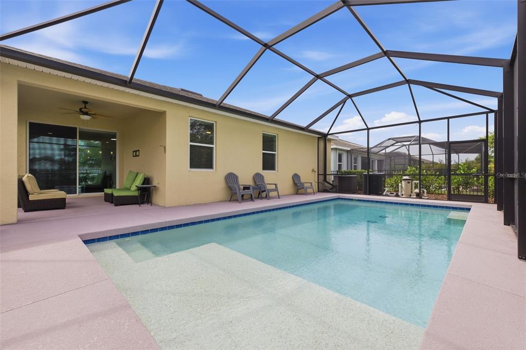 A swimming pool with a screened-in lanai and patio furniture sits behind a house — 7533 LANTERN PARK AVENUE, APOLLO BEACH, FL