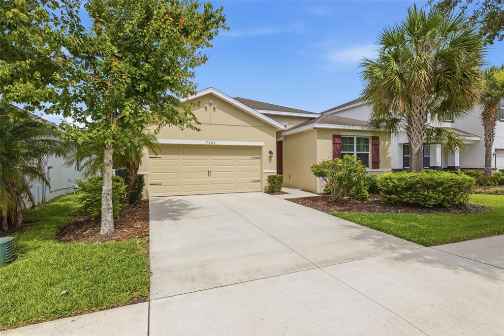 A tan single-story house with a two-car garage, palm trees, and a concrete driveway — 7533 LANTERN PARK AVENUE, APOLLO BEACH, FL