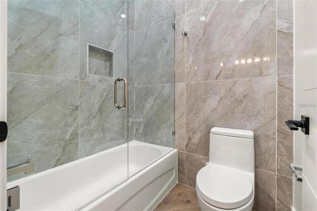 A bathroom features a white bathtub with a glass door and gray marble-look tile walls — 403 PARK BLVD, OLDSMAR, FL