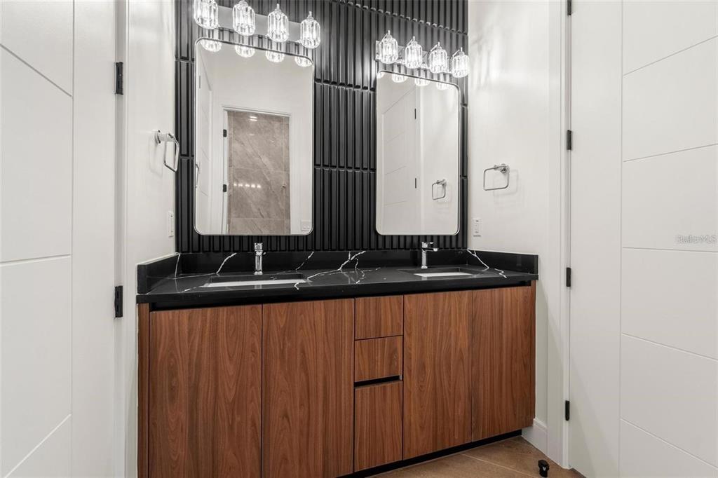 A modern bathroom features a double vanity with wood cabinets, black countertops, and vertical tile — 403 PARK BLVD, OLDSMAR, FL