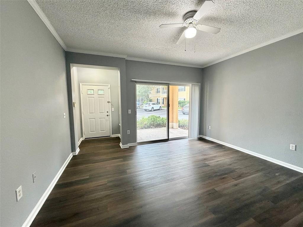 An empty living room features gray walls, dark wood-look flooring, a ceiling fan, and sliding doors — 413 ARBOR LAKES CIRCLE UNIT 413, SANFORD, FL