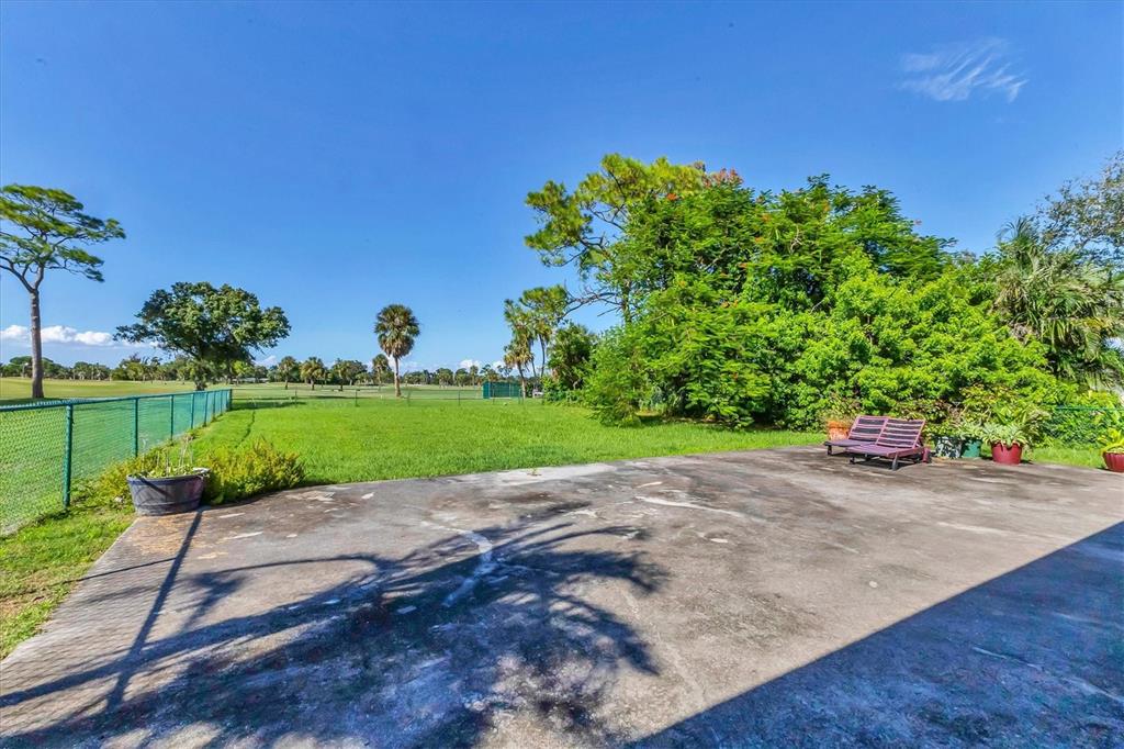A concrete patio overlooks a grassy lawn with trees and a fenced golf course — 4704 18TH AVENUE W, BRADENTON, FL