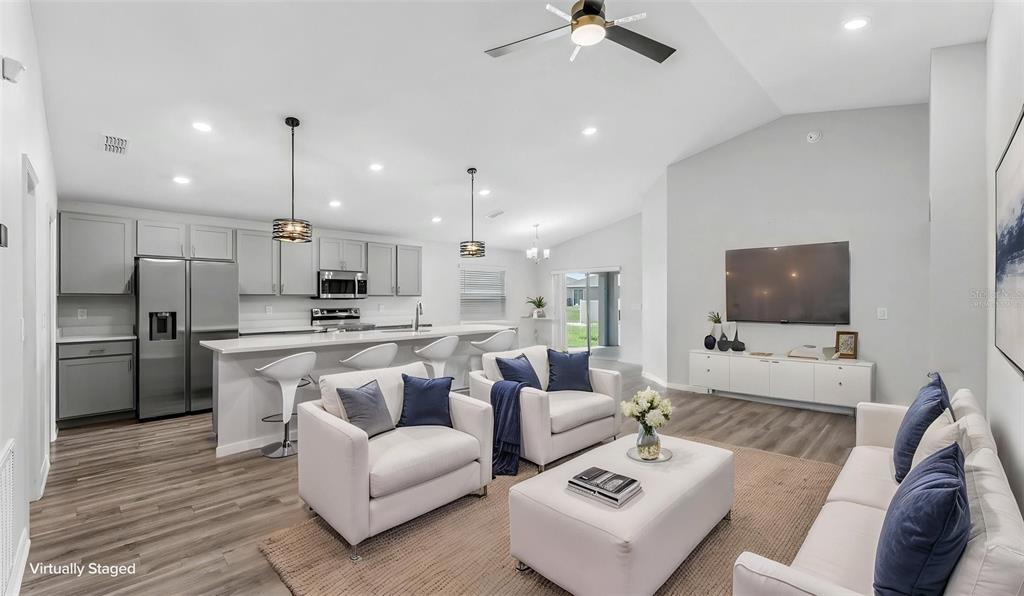 An open-concept living room and kitchen featuring gray cabinetry, stainless appliances, and wood-look flooring — 2638 SAN MARCO WAY, WINTER HAVEN, FL