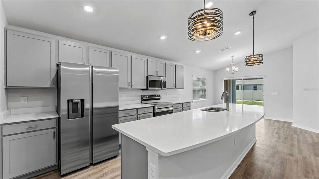 A modern kitchen features gray cabinets, stainless steel appliances, a white island, and wood flooring — 2638 SAN MARCO WAY, WINTER HAVEN, FL