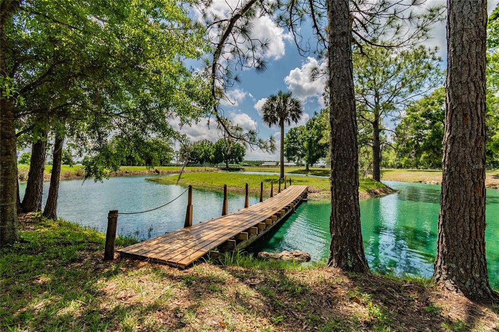 A wooden footbridge crosses a turquoise pond toward a grassy island under a blue sky — 6225, 6229 DEEN STILL ROAD, LAKELAND, FL