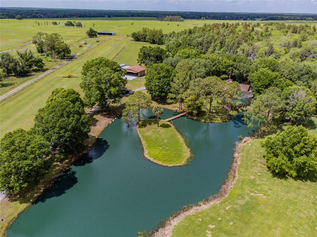 An aerial view shows a pond with a small island, a house, and a hangar — 6225, 6229 DEEN STILL ROAD, LAKELAND, FL