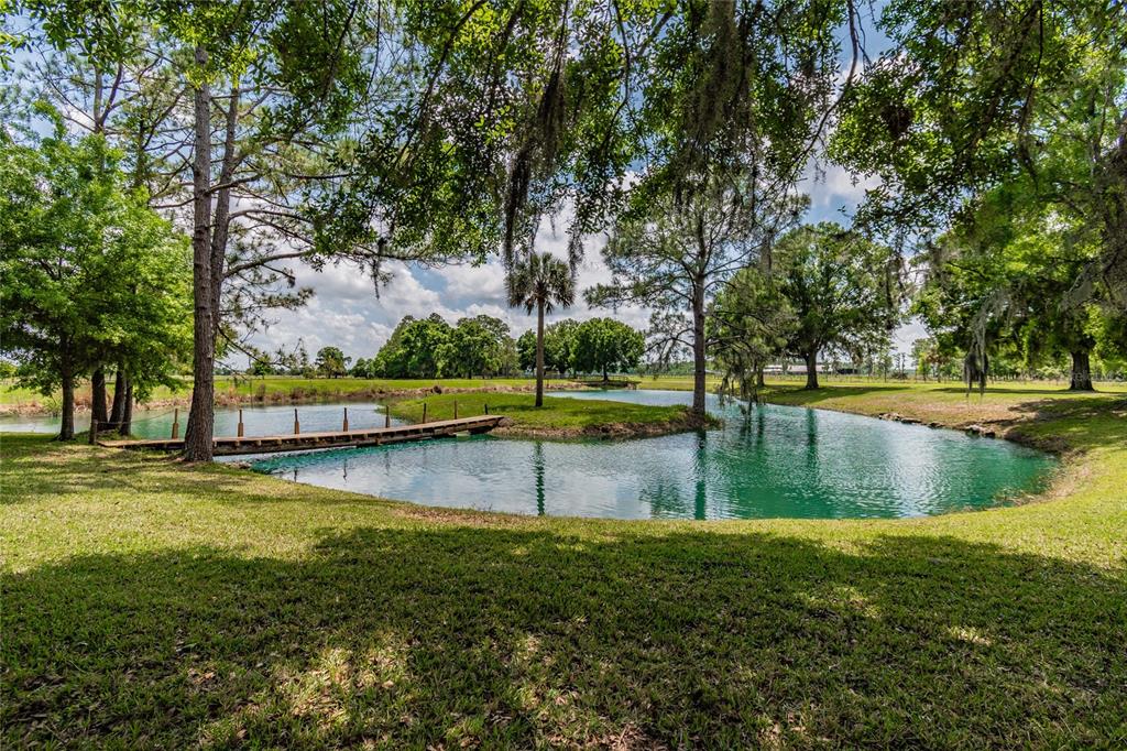 A wooden footbridge crosses a pond surrounded by grassy lawns and mature trees — 6225, 6229 DEEN STILL ROAD, LAKELAND, FL